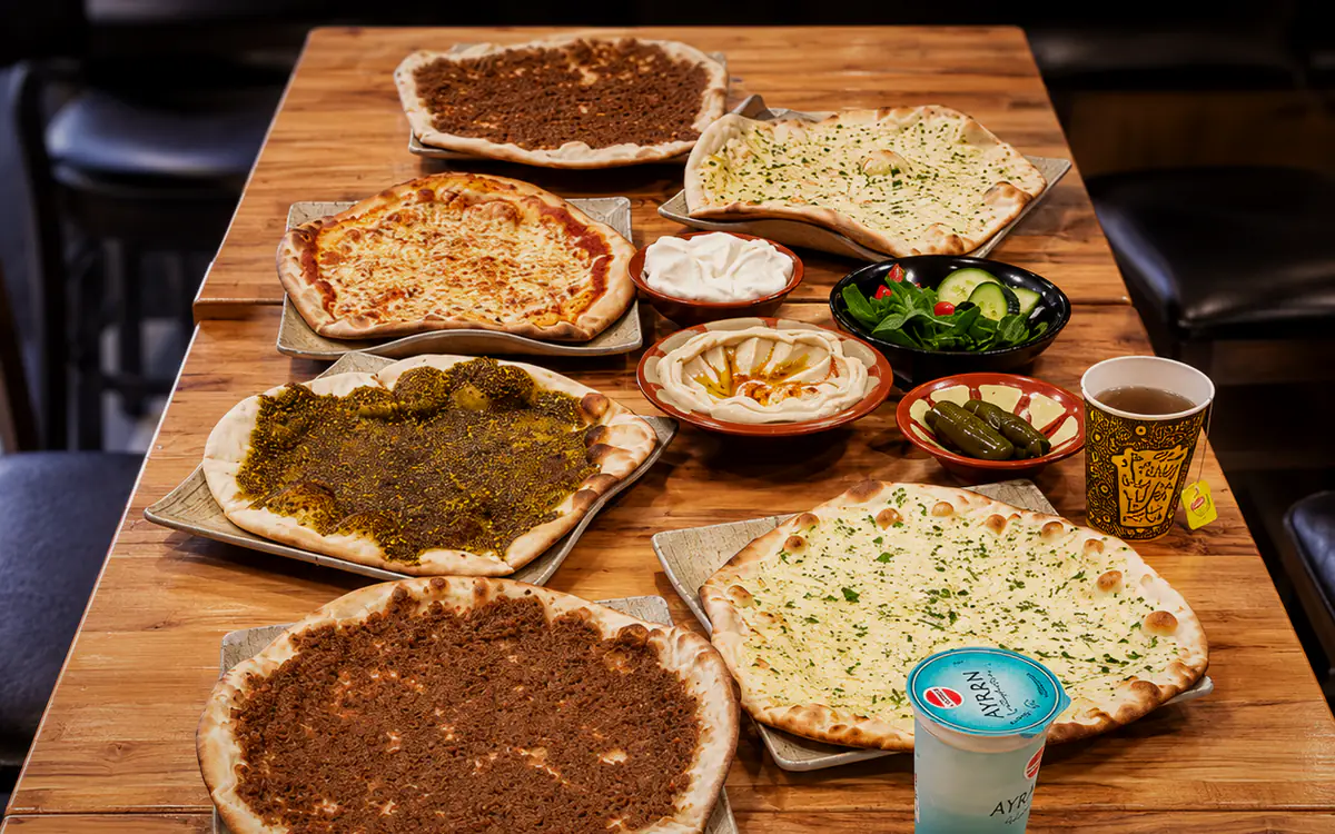 A laid table of manakish, cheese breads, zaatar, meat breads, hummus and pickles.