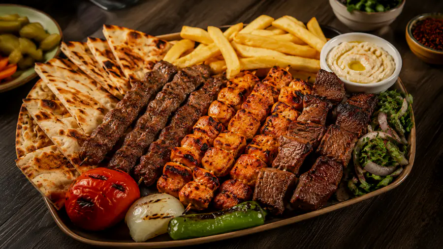 Grill platter with kebab, shish taouk and grilled meat cubes, served with bread, grilled tomato and onion.