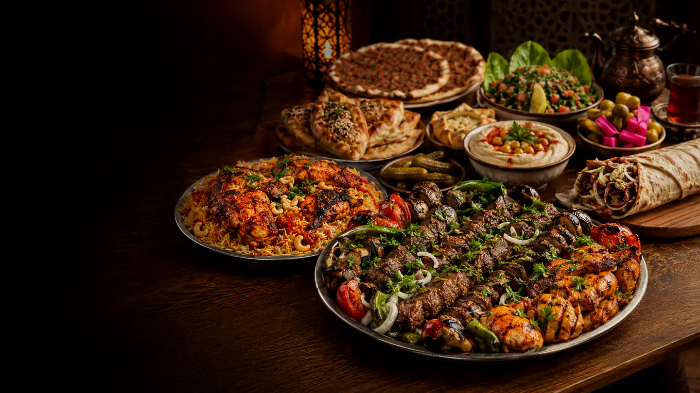 A laid Syrian table with a mixed grill platter, grilled chicken with coloured seasoned rice, shawarma, lahm bi ajeen, small pastries, hummus, tabbouleh, pickles and tea.