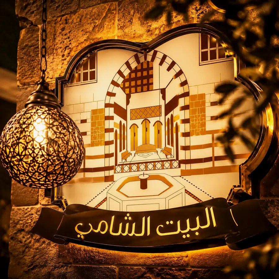 The illuminated البيت الشامي sign inside the restaurant.